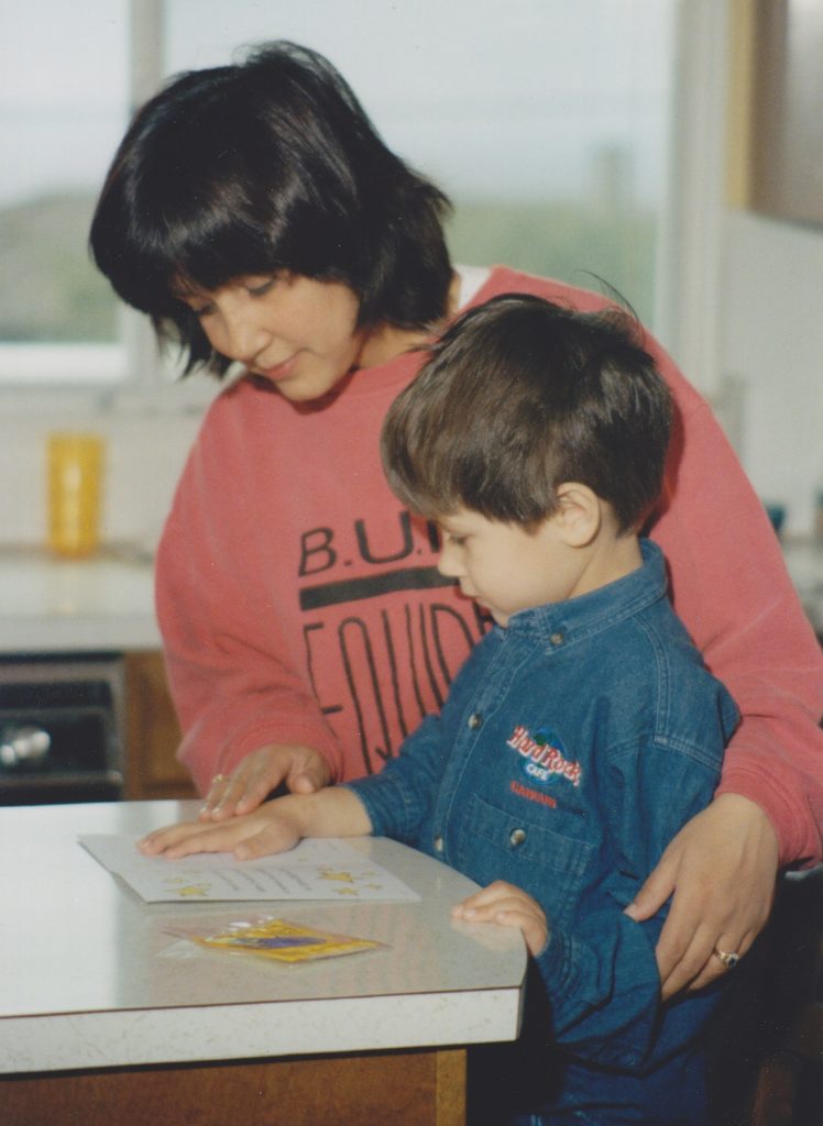 A Mother and young son standing at the kitchen counter pressing the boy's hand on a card, making a handprint footprint keepsakes for parents