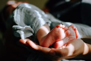 The cute feet inspire making baby footprints as keepsakes for parents. An adult's hand supports a baby's feet close up,